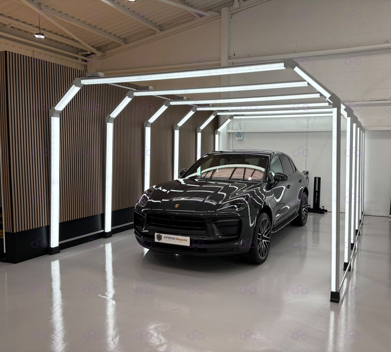 A black Porsche SUV parked inside a modern white LED light tunnel on a polished gray floor, with a slatted wood wall on the left.