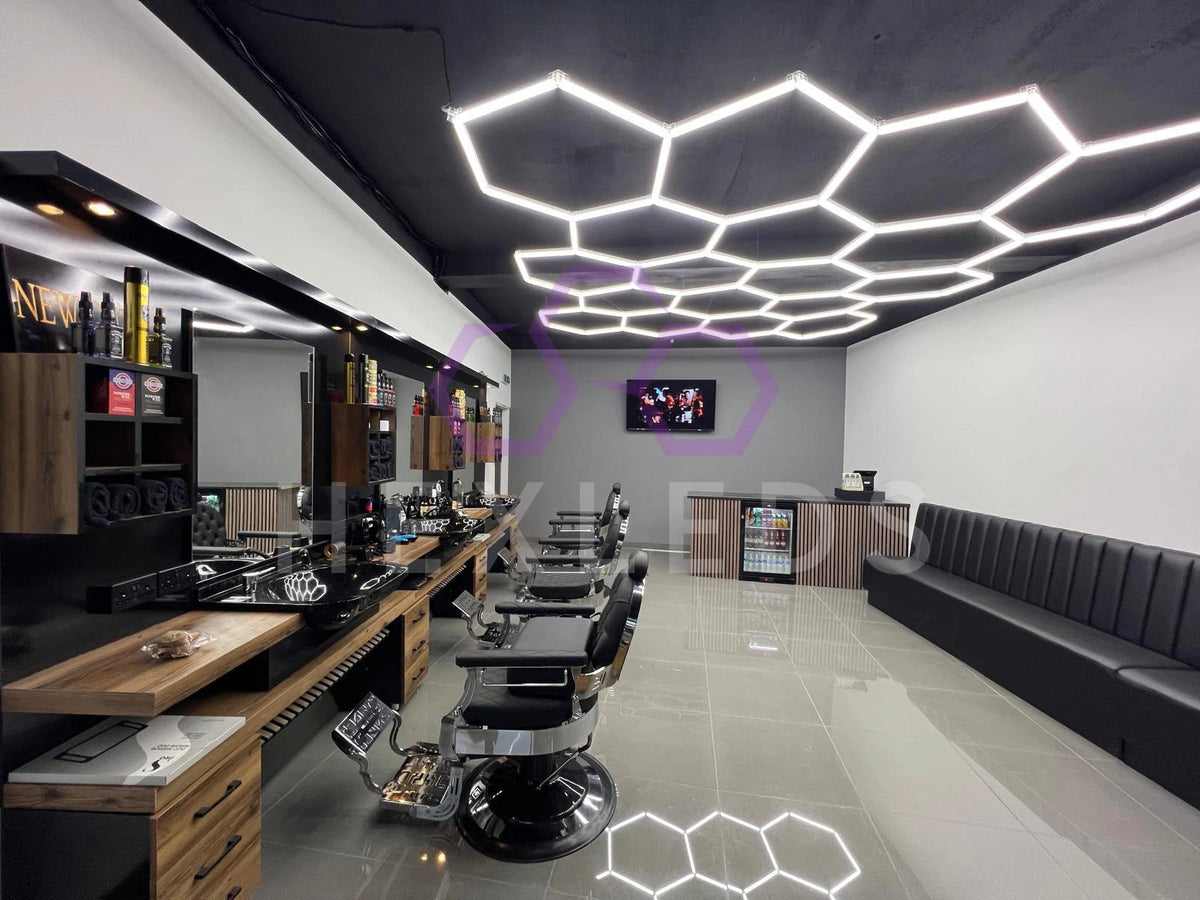 Modern barbershop interior with black chairs, wooden counters, and hexagonal ceiling lights.