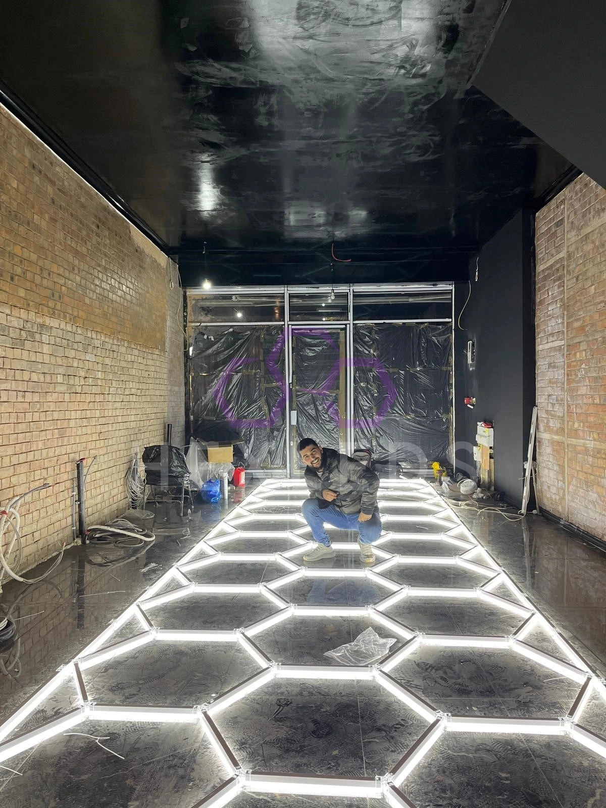 Person inspecting a newly installed black hexagonal tile floor with white grout in a room with brick walls and a black ceiling.